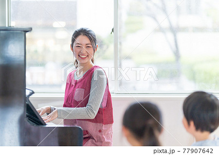 ピアノを弾く保育士と歌う園児 ピアノを弾く保育士と歌う園児 77907642