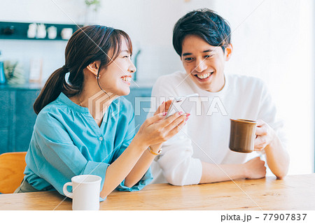 一緒にスマホを見る若い夫婦 カップル 77907837