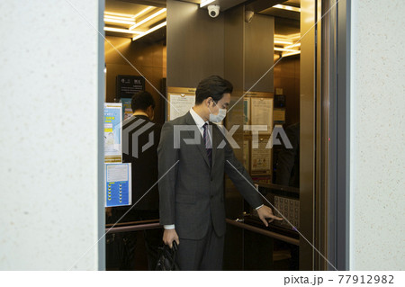 Asian business man in suit wearing mask in elevator 77912982