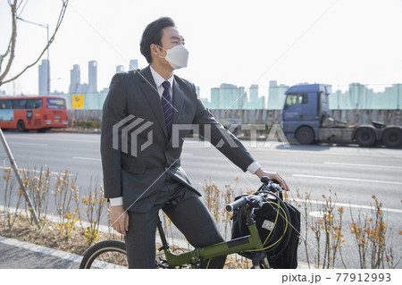 Asian man in smart casual suit wearing mask on bicycle, on the way to work Asian man in smart casual suit wearing mask on bicycle, on the way to work 77912993