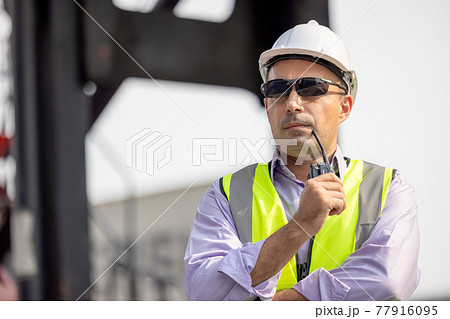 Man Using Walkie Talkie At Container Terminal, Industrial worker is controlling container loading 77916095