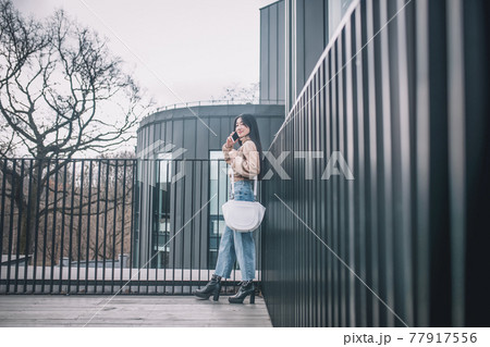 Woman in jeans and beige blouse walking and talking on the phone 77917556