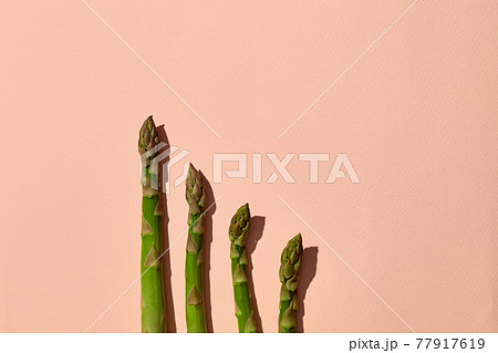 Uncooked green asparagus spears on pink background. Concept of healthy nutrition, food and seasonal vegetables harvest. Close up, copy space Uncooked green asparagus spears on pink background. Concept of healthy nutrition, food and seasonal vegetables harvest. Close up, copy space 77917619