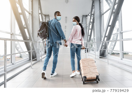 Travels During Coronavirus. Black Couple In Medical Masks Walking In Airport Terminal Travels During Coronavirus. Black Couple In Medical Masks Walking In Airport Terminal 77919429