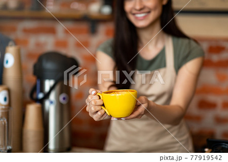 Unrecognizable female barista welcoming guests at coffee house counter, offering cup of hot beverage, closeup, crop Unrecognizable female barista welcoming guests at coffee house counter, offering cup of hot beverage, closeup, crop 77919542