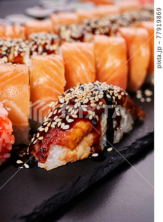 One piece of nigiri sushi lies on a black stone board on a background of rolls Philadelphia. One piece of nigiri sushi lies on a black stone board on a background of rolls Philadelphia. 77919869