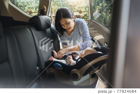 Asian young mother putting her baby son into car seat and fasten seat belts in the car Asian young mother putting her baby son into car seat and fasten seat belts in the car 77924084