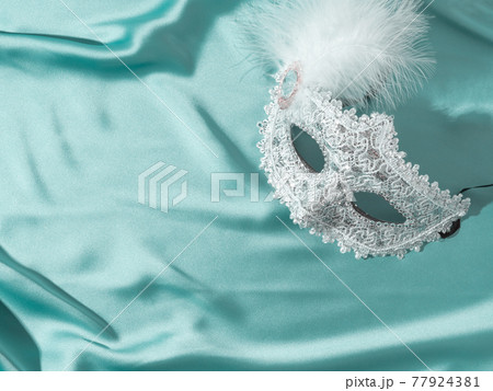 White venetian carnival mask with feather on green satin textile background White venetian carnival mask with feather on green satin textile background 77924381