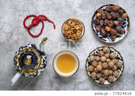 Popular food during Iftar - macadamia nuts, pistachios, walnuts, dry dates. Karan, rosary, teapot, bowl with black tea on concrete background Top view Flat lay Muslim holiday of holy month of Ramadan 77924616