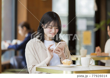 カフェでスマホを操作する若い女性 カフェでスマホを操作する若い女性 77926014