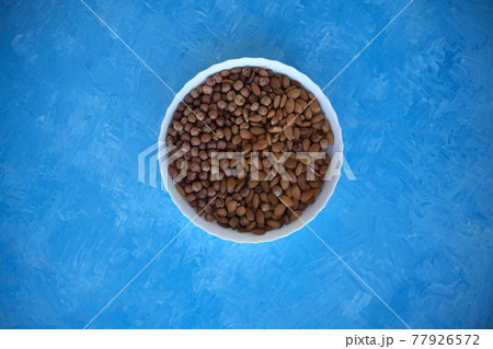 A wooden bowl with mixed nuts on top of a blue table. Healthy food and snacks. Nuts, pistachios, almonds, hazelnuts. A wooden bowl with mixed nuts on top of a blue table. Healthy food and snacks. Nuts, pistachios, almonds, hazelnuts. 77926572