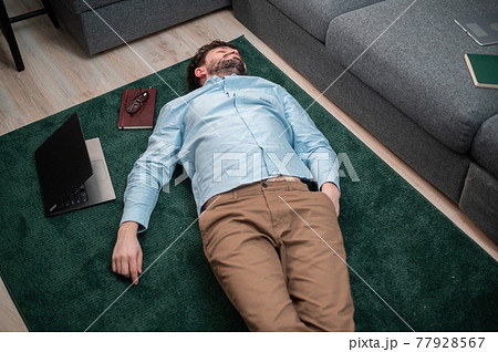 In order not to hurt his back while working, the young man decided to relax and lay down on the floor next to the sofa 77928567
