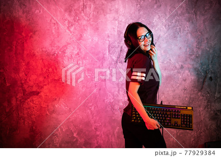 Female esports gamer posing with a gaming gear in neon light. Streamer girl standing with a gaming keyboard. 77929384