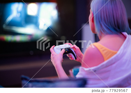 Teenager girl with colorful blue and pink hair hold joystick and play video games at home at night. 77929567
