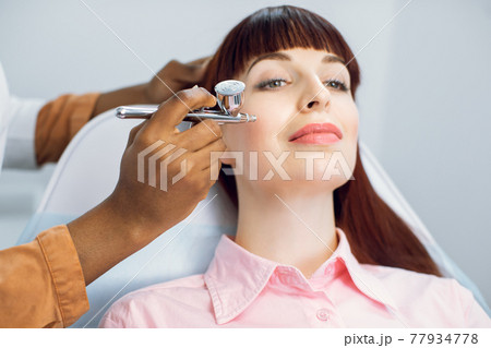 Face skin beauty treatment. Close up of likable female client getting facial gas-liquid oxygen epidermal peeling or non-injectable mesotherapy, using hardware apparatus. Face skin beauty treatment. Close up of likable female client getting facial gas-liquid oxygen epidermal peeling or non-injectable mesotherapy, using hardware apparatus. 77934778