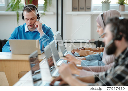 Young contact center employee working with customers complaints 77937430