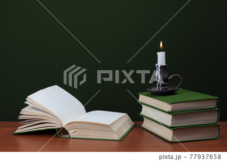open blank book and stack of books with burning candles on green background 77937658