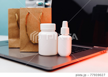 Online pharmacy. Paper bags with prescription drugs and pills and white conteiners on laptop 77939027