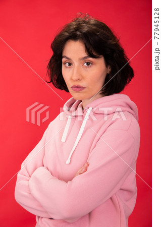 Sexy woman with crossed arms seriously looks at camera on red background Sexy woman with crossed arms seriously looks at camera on red background 77945128