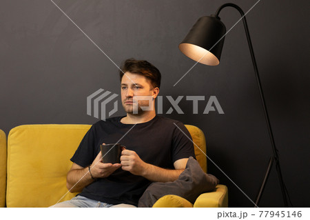 Young unshaven guy watching movie on TV on sofa with drink and remote control 77945146