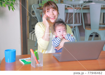 笑顔で電話するテレワークの女性とだっこされている乳児 笑顔で電話するテレワークの女性とだっこされている乳児 77946462