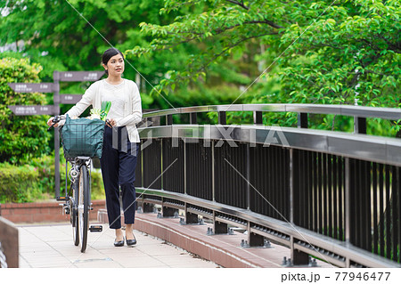 買い物袋を自転車のカゴ(籠)に入れて引いて歩く若い女性 買い物袋を自転車のカゴ(籠)に入れて引いて歩く若い女性 77946477