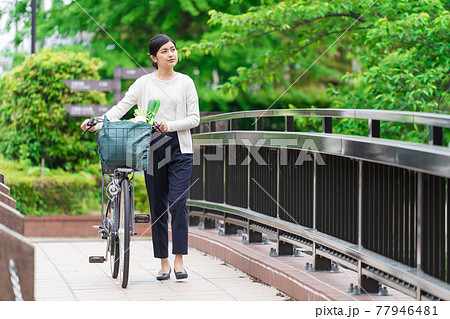 買い物袋を自転車のカゴ(籠)に入れて引いて歩く若い女性 買い物袋を自転車のカゴ(籠)に入れて引いて歩く若い女性 77946481