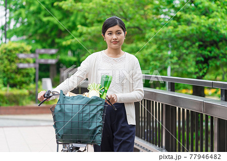 買い物袋を自転車のカゴ(籠)に入れて引いて歩く若い女性 買い物袋を自転車のカゴ(籠)に入れて引いて歩く若い女性 77946482
