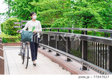買い物袋を自転車のカゴ(籠)に入れて引いて歩く若い女性 買い物袋を自転車のカゴ(籠)に入れて引いて歩く若い女性 77947627