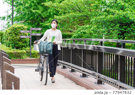 買い物袋を自転車のカゴ(籠)に入れて引いて歩く若い女性 買い物袋を自転車のカゴ(籠)に入れて引いて歩く若い女性 77947632