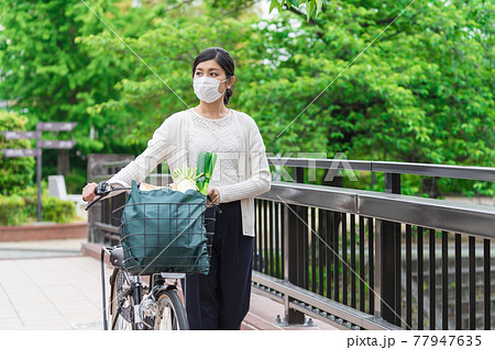買い物袋を自転車のカゴ(籠)に入れて引いて歩く若い女性 買い物袋を自転車のカゴ(籠)に入れて引いて歩く若い女性 77947635