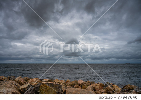 A beautiful, dramatic sky over the ocean. Stones in a wave breaker in the foreground A beautiful, dramatic sky over the ocean. Stones in a wave breaker in the foreground 77947640