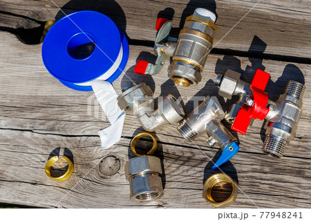 Various plumbing spare parts and sealing tape on rustic wooden background. Top view 77948241