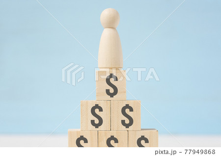 Wooden figure of man on toy blocks with painted dollar signs. Wooden figure of man on toy blocks with painted dollar signs. 77949868