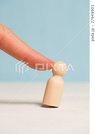 A finger pokes into a wooden figure on a blue background. Concept fired. Staff reduction. Close up. 77949901