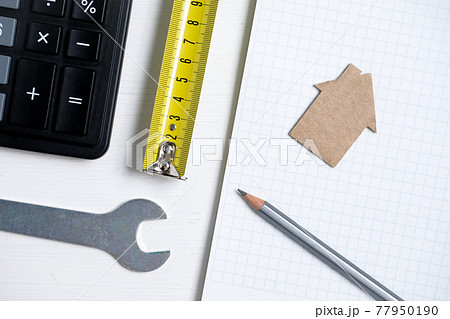 Cardboard cutout house, roulette, pencil, calculator, wrench and blank sheet of notebook. 77950190