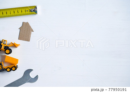 Cardboard house, wrench, roulette, toy excavator, truck on white background with copy space. 77950191