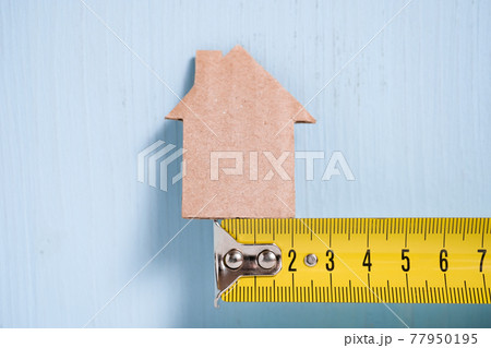 Cardboard cutout house on metal measuring tape on blue background. 77950195