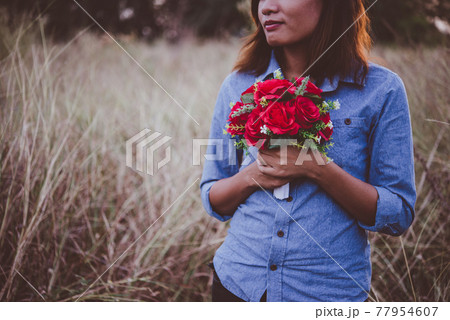 Young hipster woman in field holding a bouquet of red rose, summer holiday. Freedom enjoy lifestyle. Vintage tone. Young hipster woman in field holding a bouquet of red rose, summer holiday. Freedom enjoy lifestyle. Vintage tone. 77954607