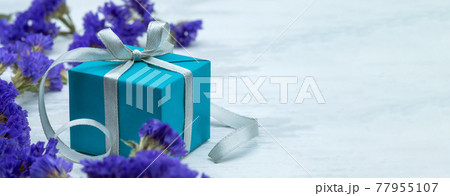 A blue box with a gray ribbon. Gift wrap and blue flowers. A blue box with a gray ribbon. Gift wrap and blue flowers. 77955107