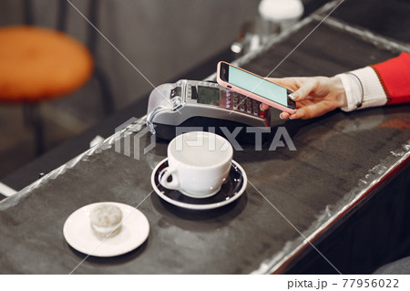 Girl paying for her latte with a smartphone by contactless PAY PASS technology Girl paying for her latte with a smartphone by contactless PAY PASS technology 77956022