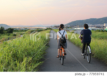 夕焼けの土手を自転車に乗る女の子 77959741