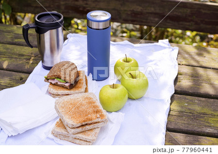 Lunch in the park on an old wooden table. Sandwiches, apples and coffee in a thermos. Lunch in the park on an old wooden table. Sandwiches, apples and coffee in a thermos. 77960441
