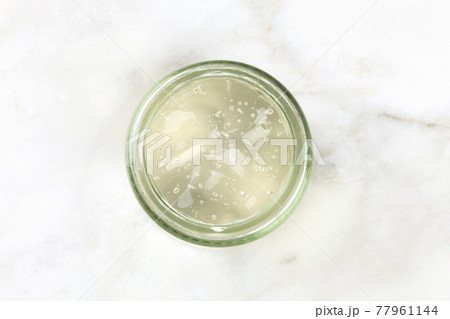 A glass jar with aloe vera gel, shot from above on a white marble background A glass jar with aloe vera gel, shot from above on a white marble background 77961144