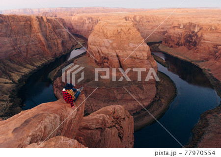 blonde girl sitting Horseshoe Bend in Glen Canyon National Recreation Area in early dawn 77970554