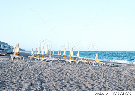 Deserted pebble beach with deck chairs and closed umbrellas in the evening. Sicily as a tourist attraction. Season on mediterranean sea. Ionian sea 77972770