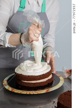 Woman hands chef spreading cream on second layer of Chocolate cake. 77972937