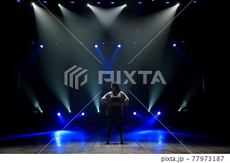 Girl in black suit performing on stage with bright blue background 77973187