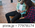 Hipster couple listening music together while sitting on bench and enjoying in urban. 77978174