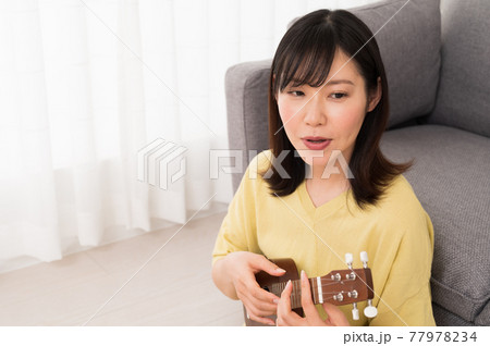 ソファーの前でウクレレを演奏する女性 ソファーの前でウクレレを演奏する女性 77978234